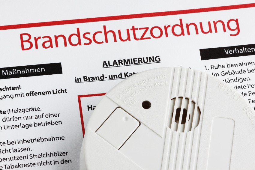 Ein Rauchmelder liegt auf einem Dokument mit der Überschrift "Brandschutzordnung"