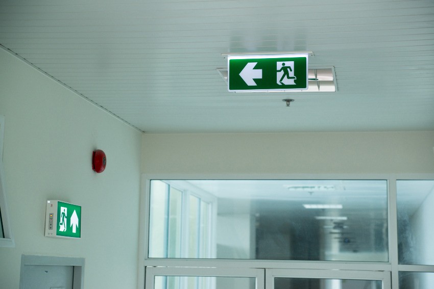 In einem Krankenhausflur sind Alarmgeber und die Kennzeichnungsschilder der Fluchtwege zu sehen 