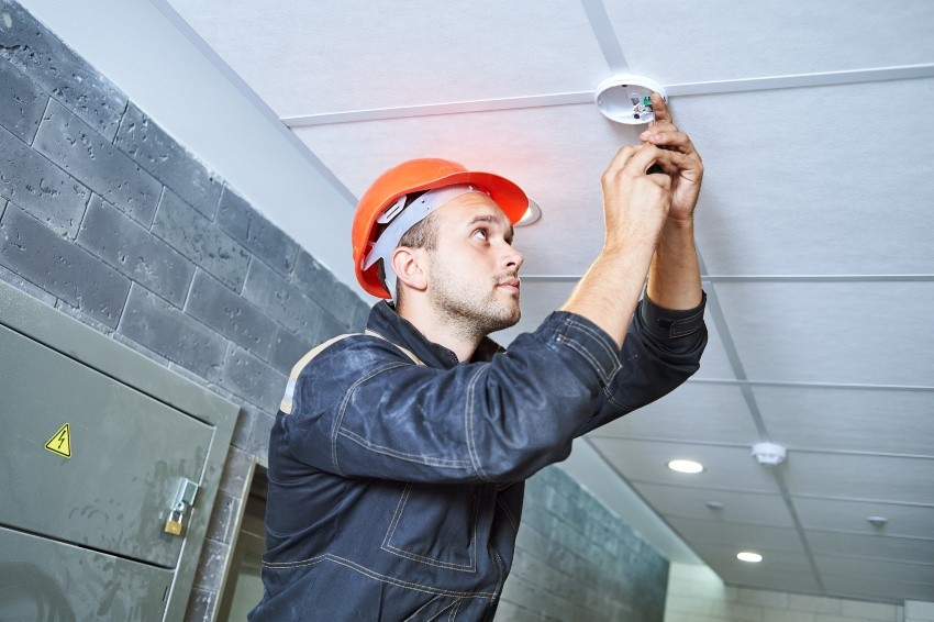 Handwerker installiert Feuer- oder Rauchmelder an der Decke